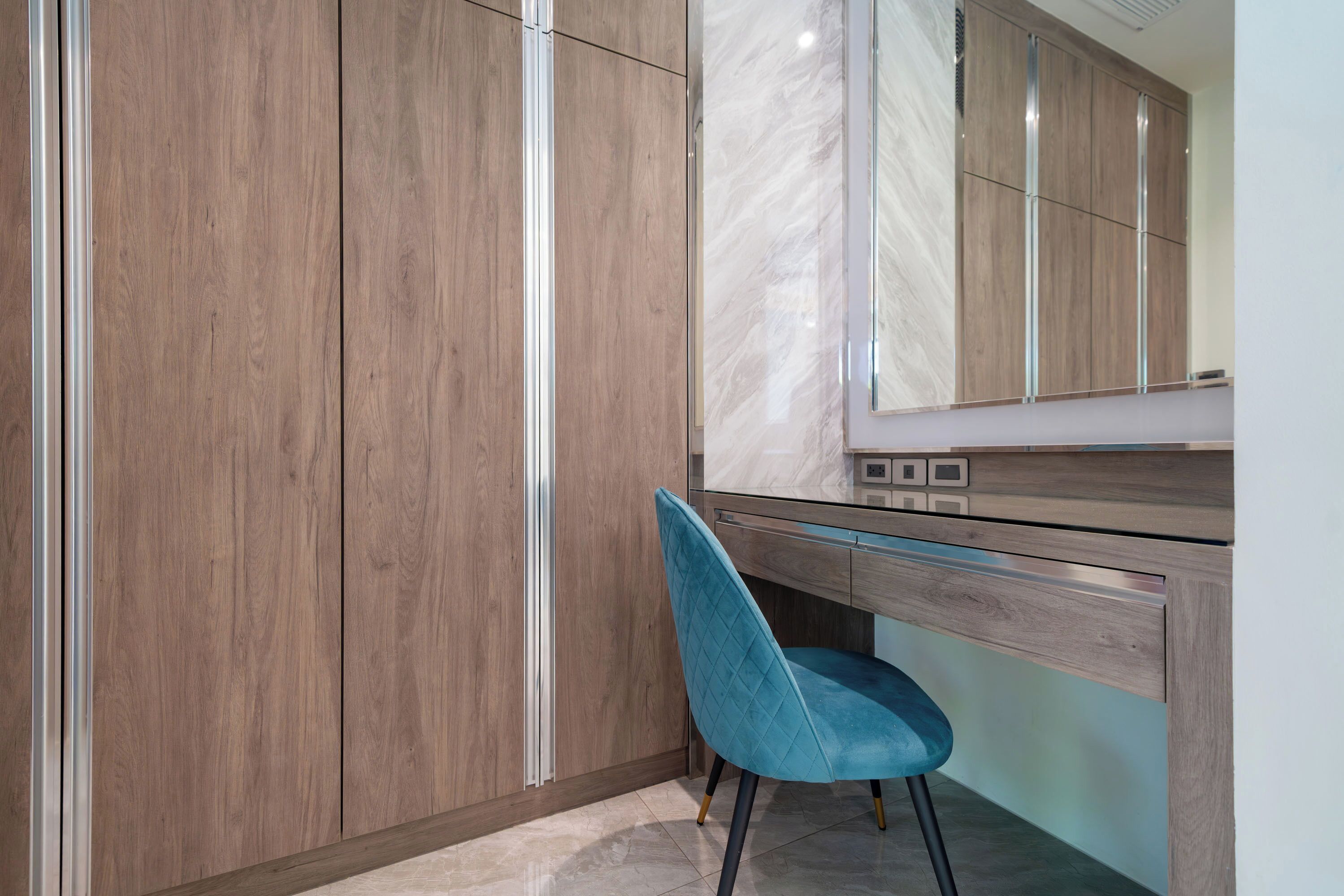 Ein modernes Badezimmer mit Holzschränken, einer Marmorarbeitsplatte und einem blauen Stuhl.
