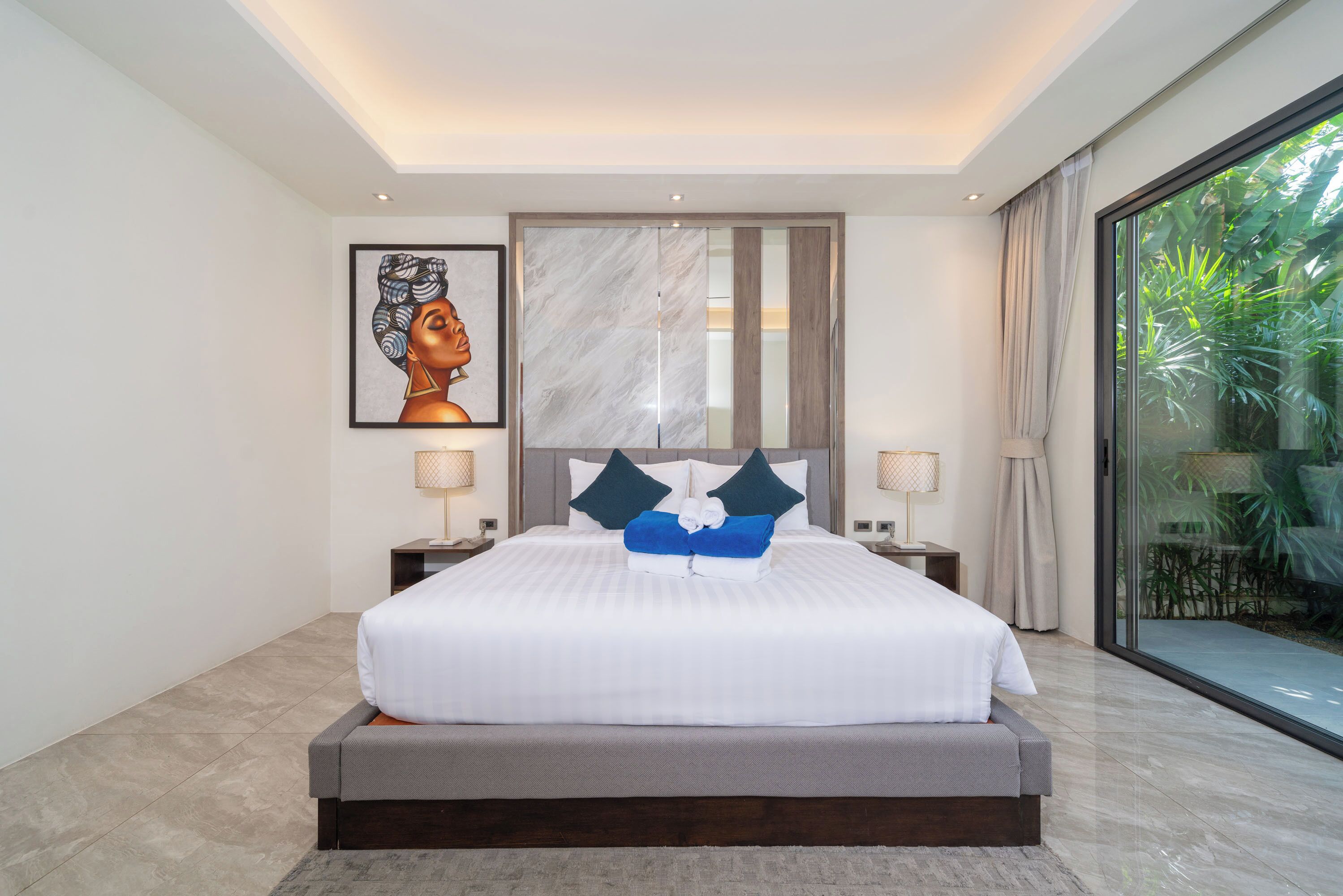 Una habitación de hotel moderna con una cama grande, cabecera de mármol, un amplio ventanal con vistas a zonas verdes y una obra de arte enmarcada en la pared.