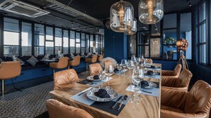 A dining area with a long table set for a meal, leather chairs, and pendant lighting. - Chic N Cozy Citygate 1Br Suite (Kamala)