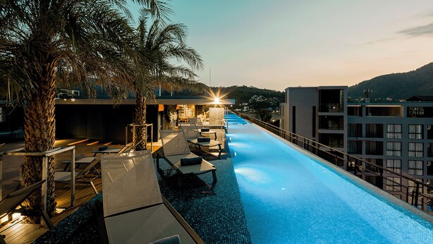 A swimming pool with lounge chairs and a palm tree, surrounded by buildings. - Citygate Kamala 1Br Oasis Suite (Kamala)