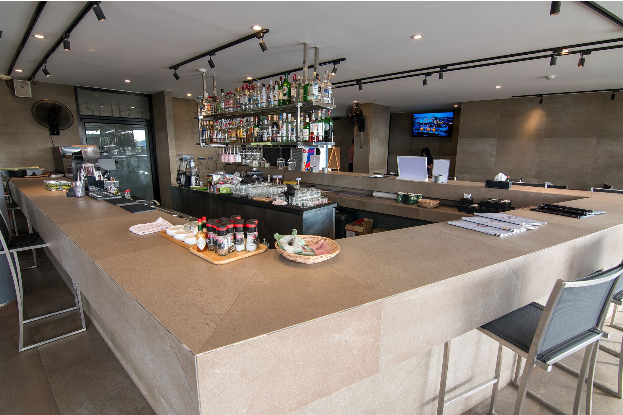 Un bar moderne doté d’un long comptoir, d’étagères remplies de bouteilles d’alcool et d’un écran de télévision en arrière-plan.