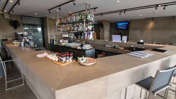 A modern bar area with a long counter, shelves of liquor bottles, and a television screen in the background.