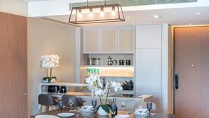 Un espace repas moderne avec une table en bois dressée pour quatre personnes, un vase d’orchidées blanches et, au fond, une cuisine avec des armoires blanches et un plan de travail.