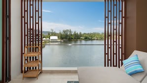 A balcony with a view of a lake, a sofa with a striped pillow, and a wooden shelf. - Angsana Lakeside Luxury 2Br Jazuzzi Suite (Choeng Thale)