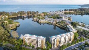 Une station balnéaire dotée d’un lac central, relié par des passerelles, entourée d’une végétation luxuriante et de bâtiments modernes avec balcons.