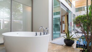 A modern bathroom with a large freestanding bathtub, a potted plant, and a view of the pool area. - Mahogany 4Br Pool Villa In Bangtao (Choeng Thale)