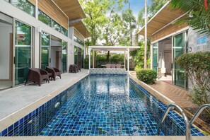 A swimming pool with blue mosaic tiles, surrounded by a covered seating area with chairs and a table. - Mahogany 4Br Pool Villa In Bangtao (Choeng Thale)