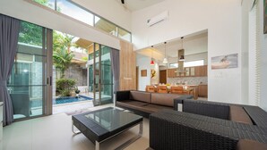 A modern living room with a glass coffee table, a sofa, and a dining area with wooden furniture. - Mahogany 4Br Pool Villa In Bangtao (Choeng Thale)