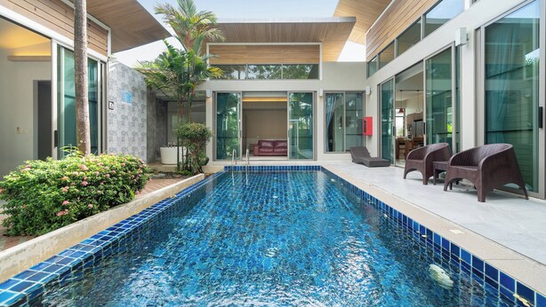 A modern indoor pool with clear blue tiles, surrounded by glass walls and wooden ceiling. - Mahogany 4Br Pool Villa In Bangtao (Choeng Thale)