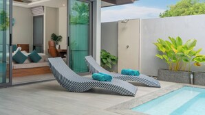 A modern outdoor pool area with two lounge chairs, a glass-enclosed room, and a potted plant. - Nicky Elegant 3Br Pool Villa Bangtao (Choeng Thale)
