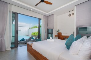 Ein modernes Hotelzimmer mit einem großen Bett, einem Deckenventilator, einem Schreibtisch mit Stuhl und Blick auf einen Swimmingpool und Grünflächen.