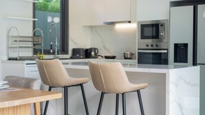 A modern kitchen with two bar stools, a wooden table, and a large window. - Nicky 3Br Private Pool Villa Bangtao (Choeng Thale)