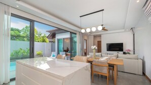 A modern living room with a dining area, a large TV, and a view of a swimming pool. - Nicky 3Br Private Pool Villa Bangtao (Choeng Thale)