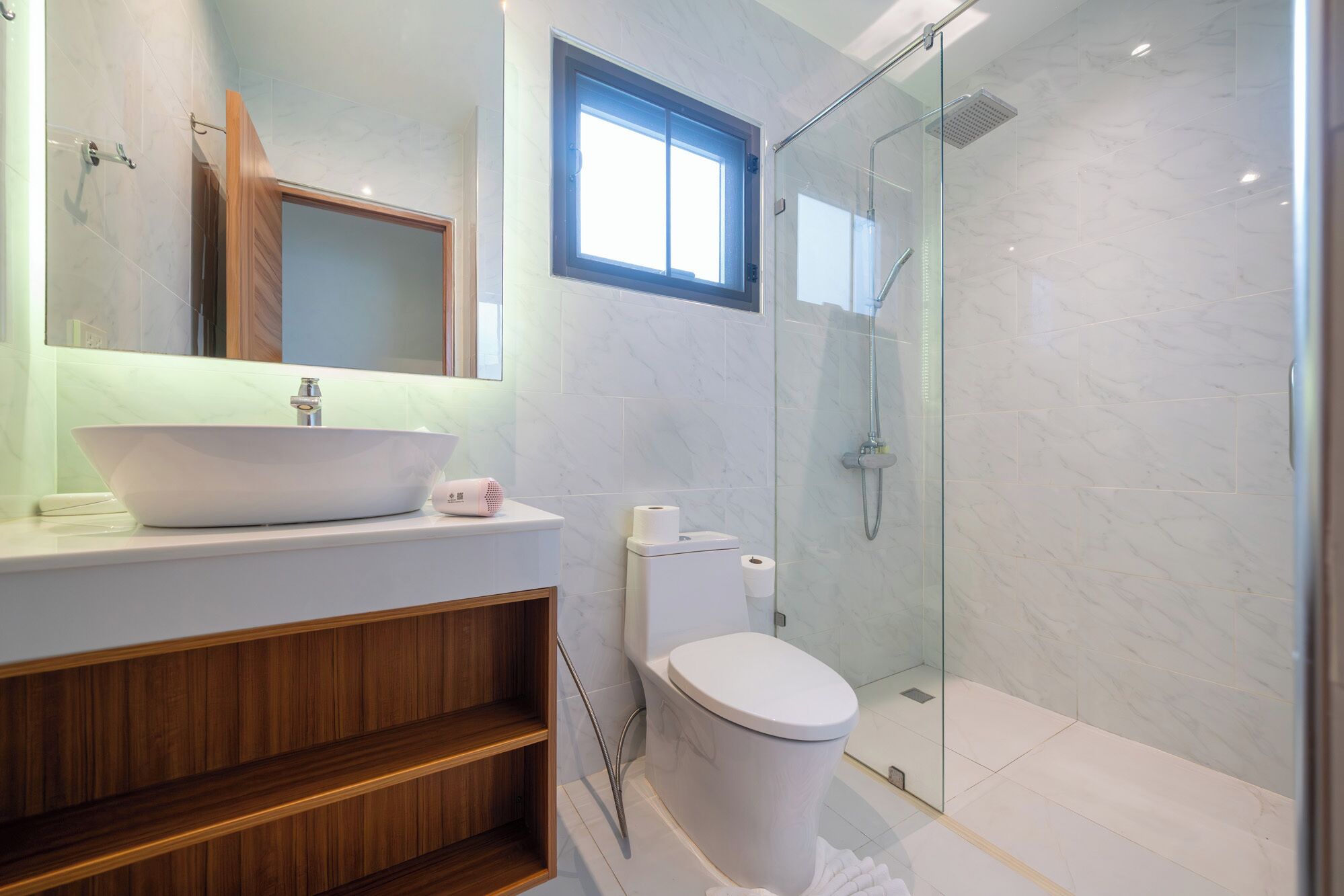Un baño moderno con un lavamanos grande de color blanco, un inodoro y una ducha con cerramiento de vidrio.