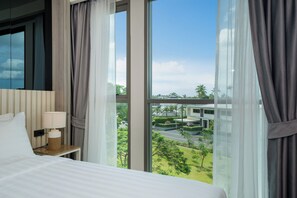 A hotel room with a large window, a bed, a bedside table with a lamp, and a view of a building and greenery outside. - Ozone 1Br Condo In Excellent Laguna Area (Choeng Thale)