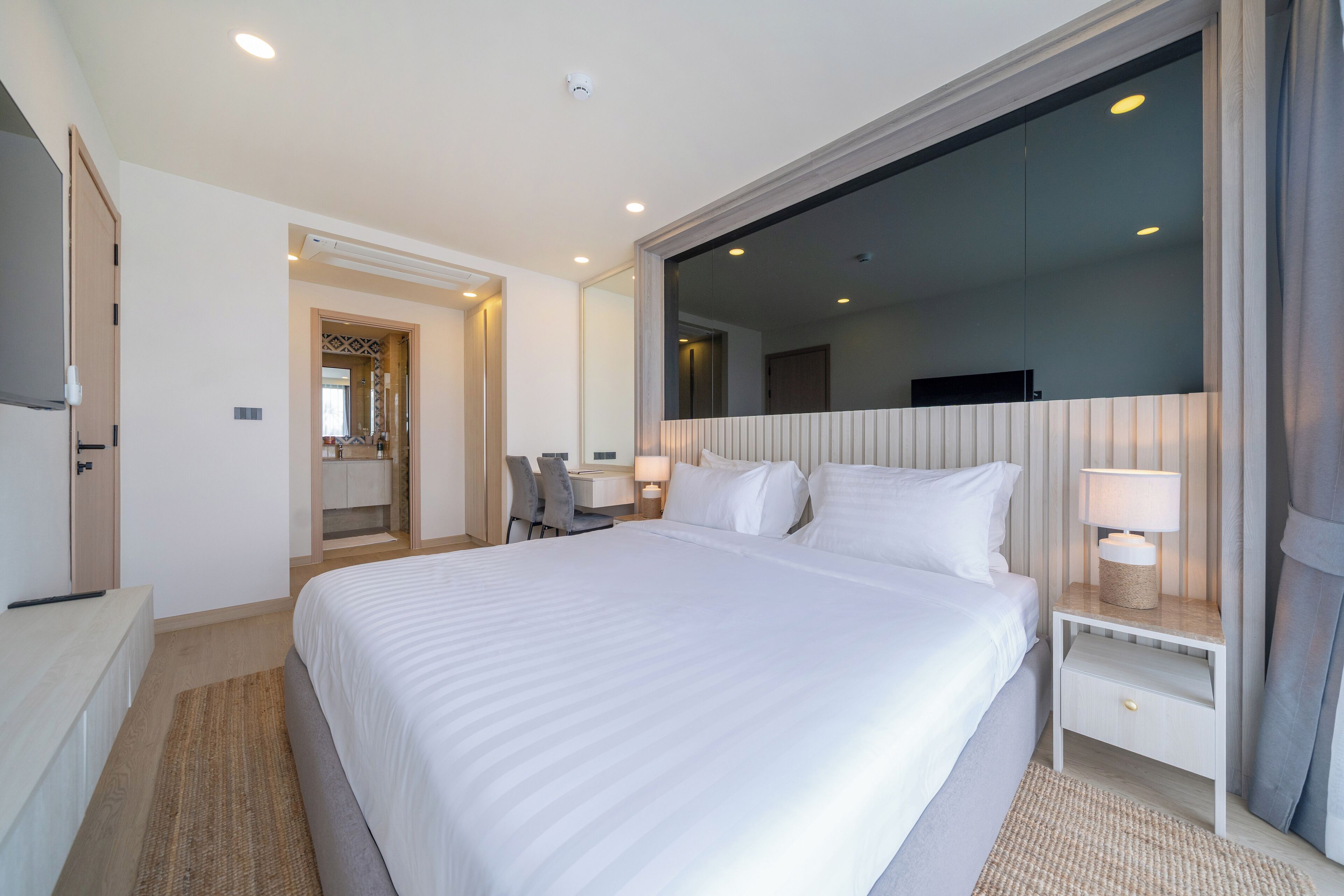 A hotel room with a large bed, a desk with a chair, a TV, and a mirror.