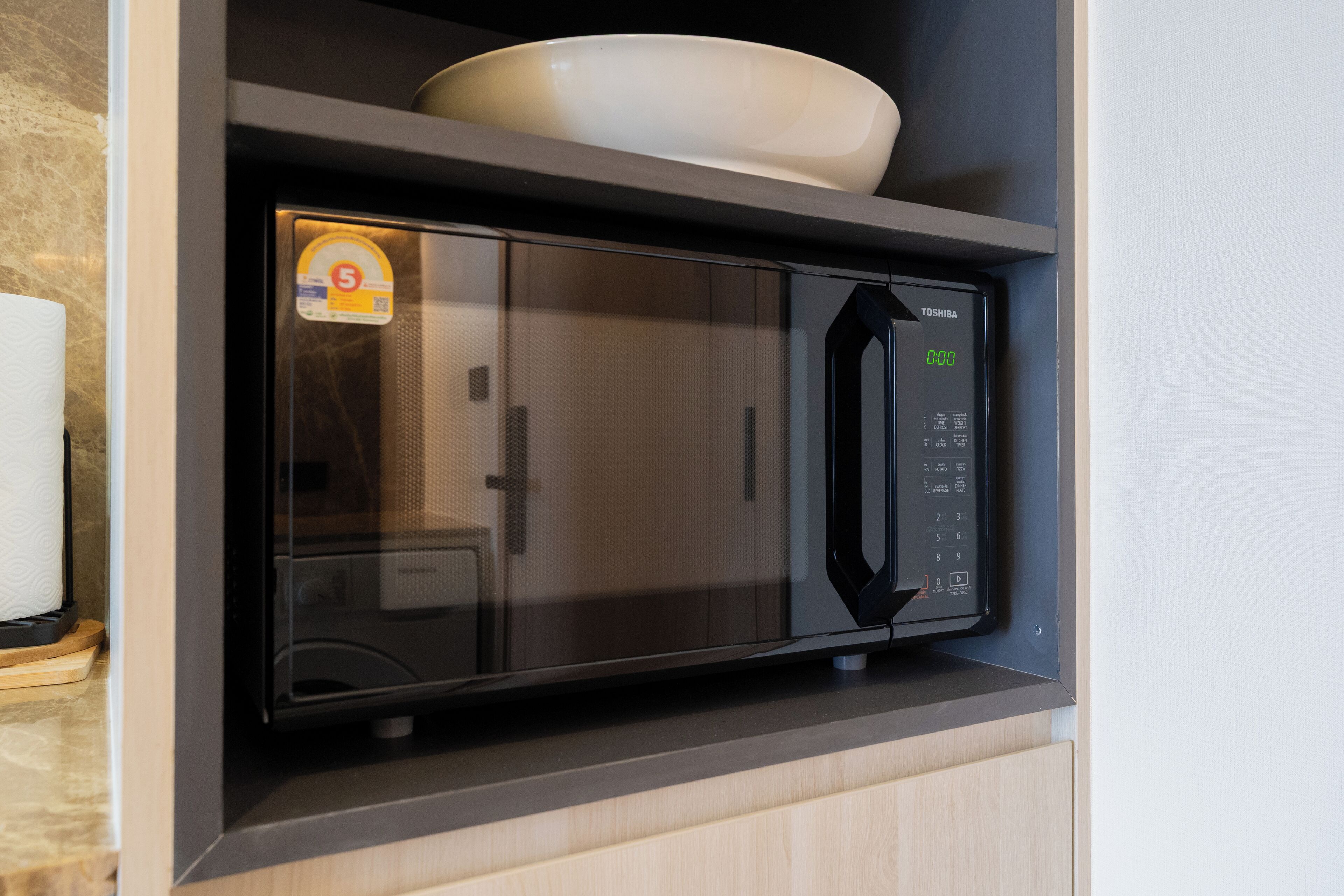 Un forno a microonde nero con display digitale e pannello di controllo, inserito in un pensile da cucina con piano di lavoro in legno.