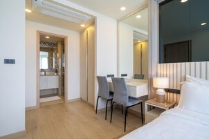 A hotel room with a bed, a desk with two chairs, a small table with a lamp, and a large mirror.
