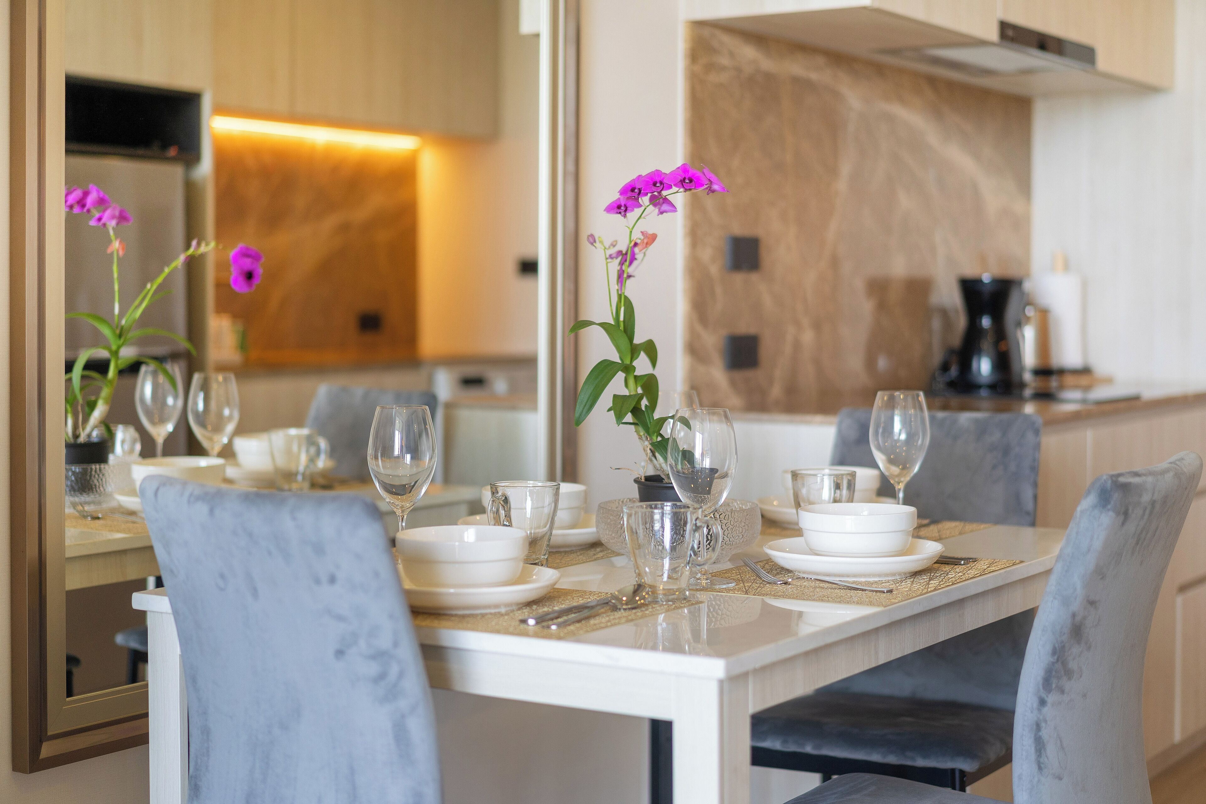 A dining area with a marble countertop, white plates, clear glasses, and a vase with purple flowers.