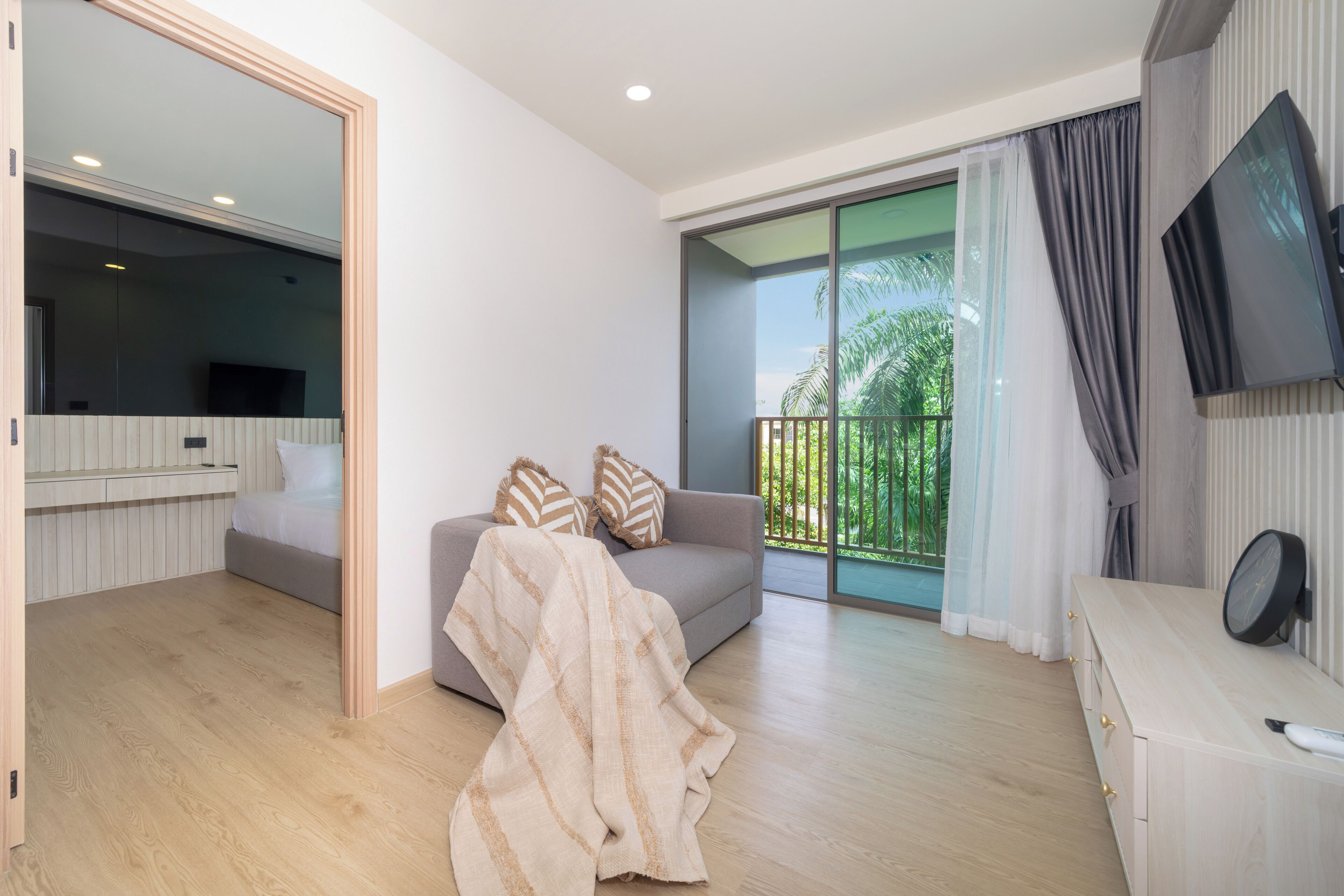 A modern living room with a sofa, a TV, and a balcony with a view of greenery.