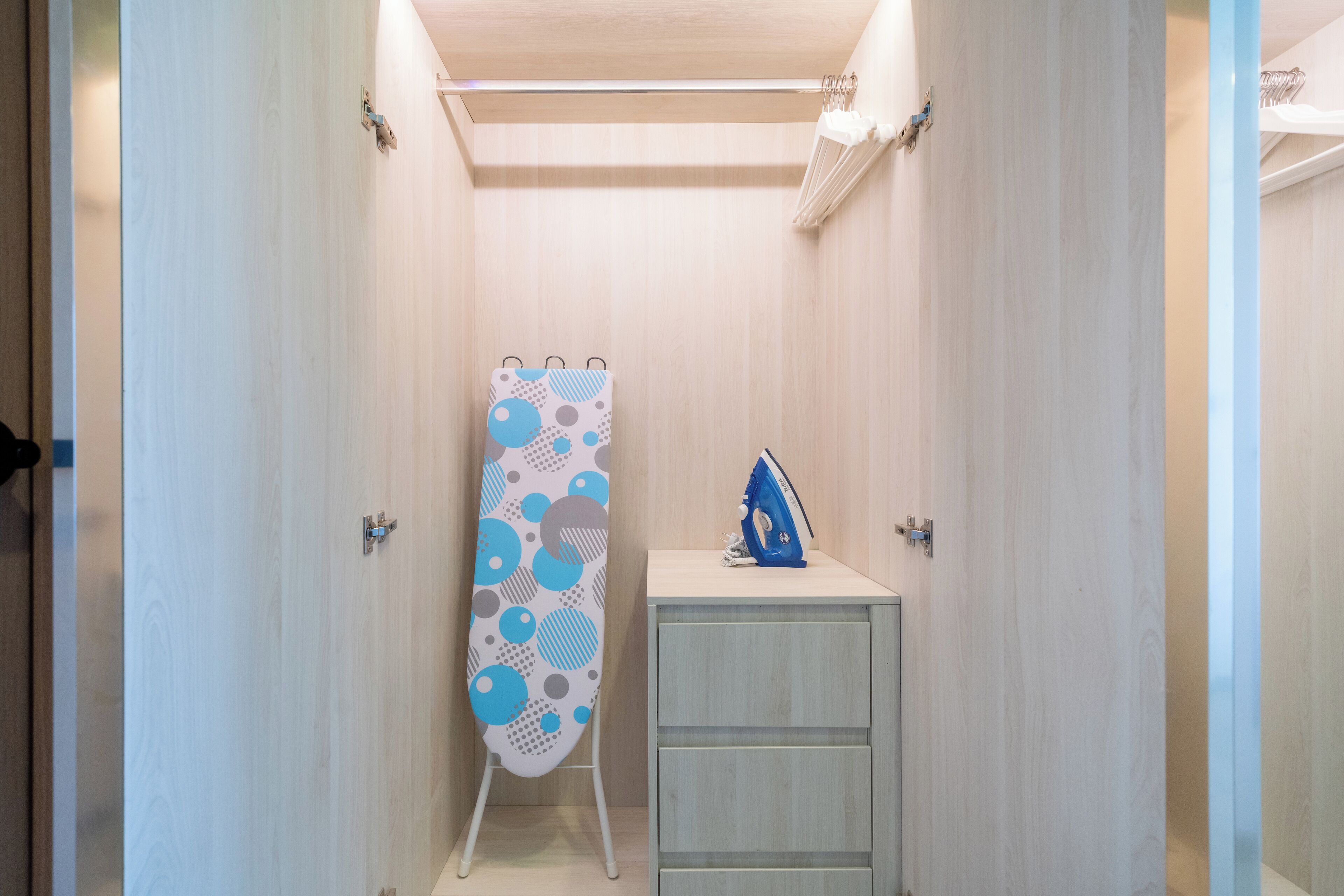 Ein schmaler Korridor mit Holzboden und Wänden, eine Tafel mit blau-grauem Muster sowie ein kleiner, weißer Schrank mit einem blauen Gegenstand darauf.