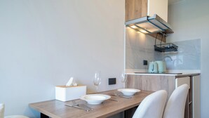 A modern dining area with a wooden table, white chairs, and a kitchen area with a built-in stove and kettle. - Space Cherngtalay In Elegant Bangtao (Choeng Thale)