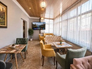 Eine Hotlellobby mit Holzboden, einem Flachbildfernseher an der Wand und einer Sitzecke mit Stühlen und Tischen.