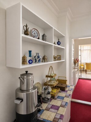A kitchen with white shelves holding decorative items, a stainless steel kettle, and a checkered floor. - Galley Port (Istanbul)