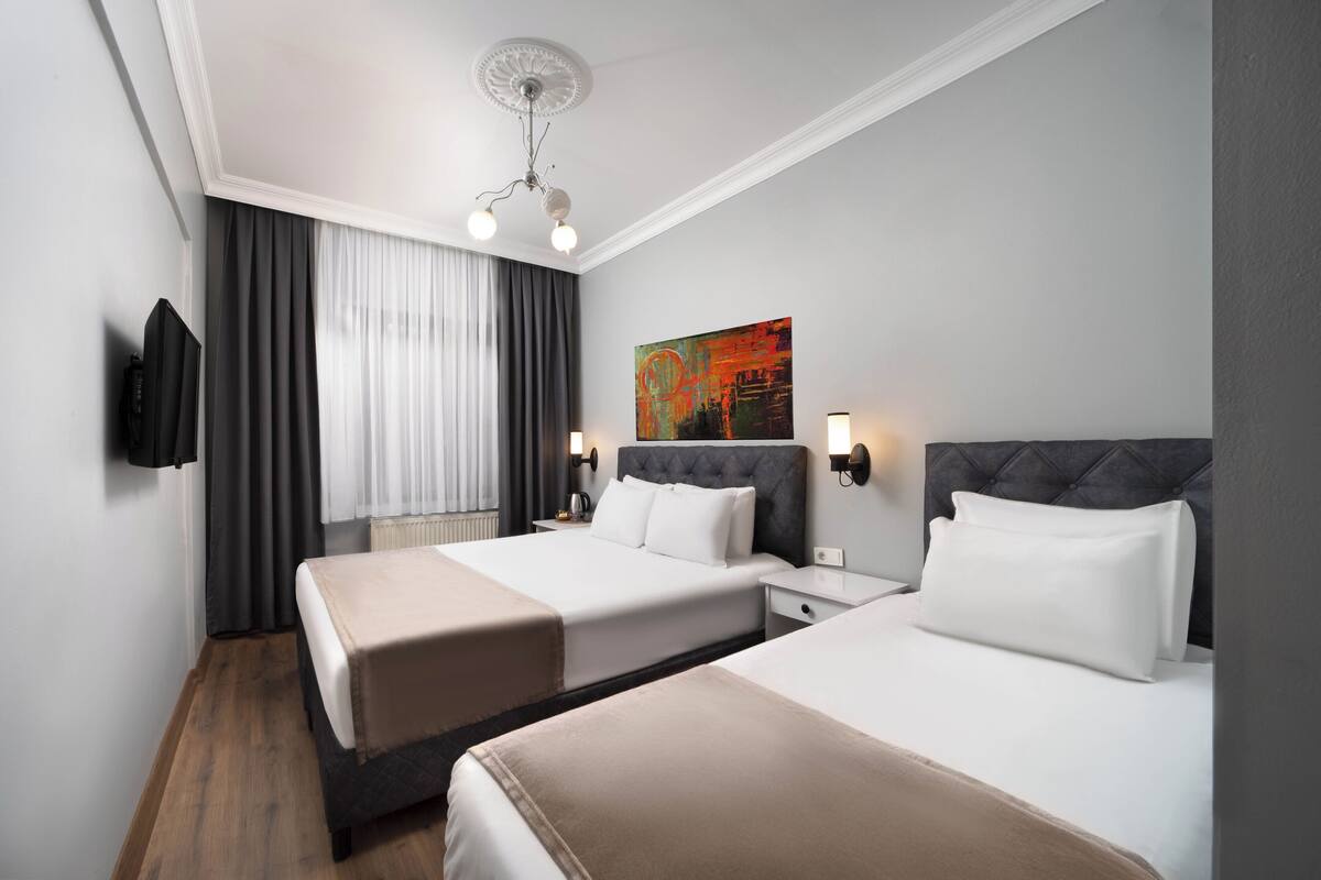 Ein Hotelzimmer mit zwei Betten, einem Fernseher, einem Gemälde und einem Deckenventilator.