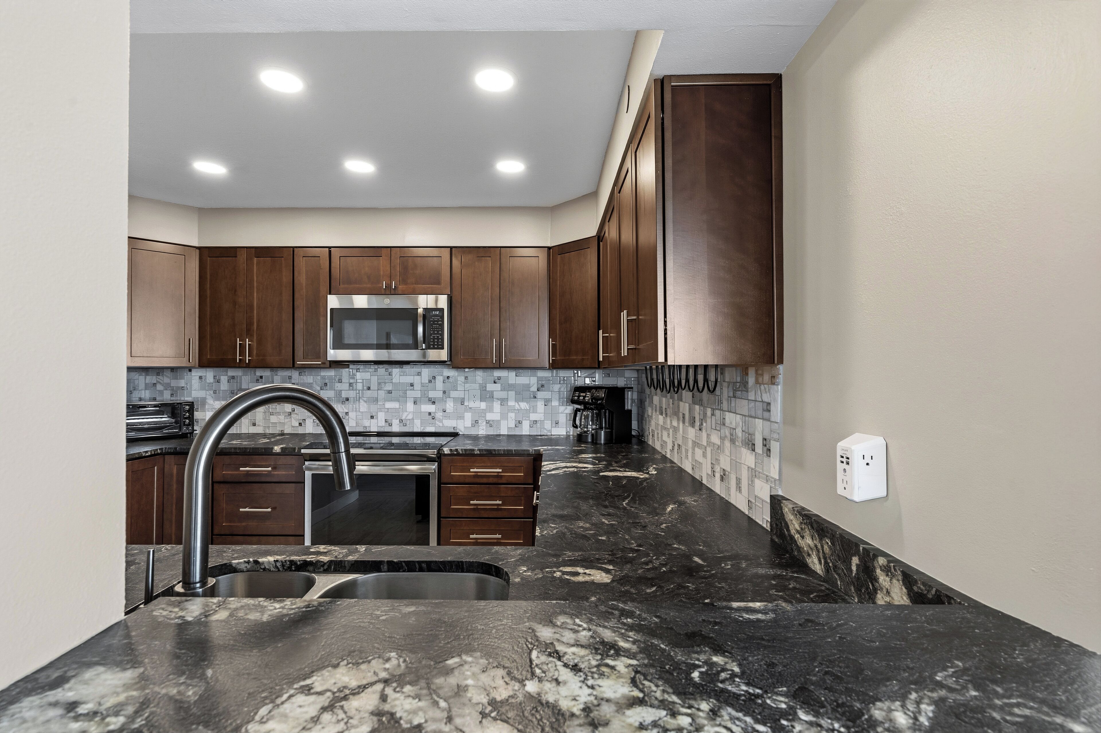A modern kitchen with dark wooden cabinets, a stainless steel sink, and a tiled backsplash.
