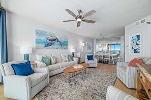 A spacious living room with a ceiling fan, a large painting, and a dining area in the background. - Windward Pointe 1502 | Beachfront | Pools | Tennis & Pickleball | My Beach Getaways (Orange Beach)