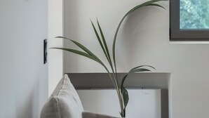 Un saló modern amb un sofà gris, una taula auxiliar petita amb una planta i una finestra gran amb vista a arbres.