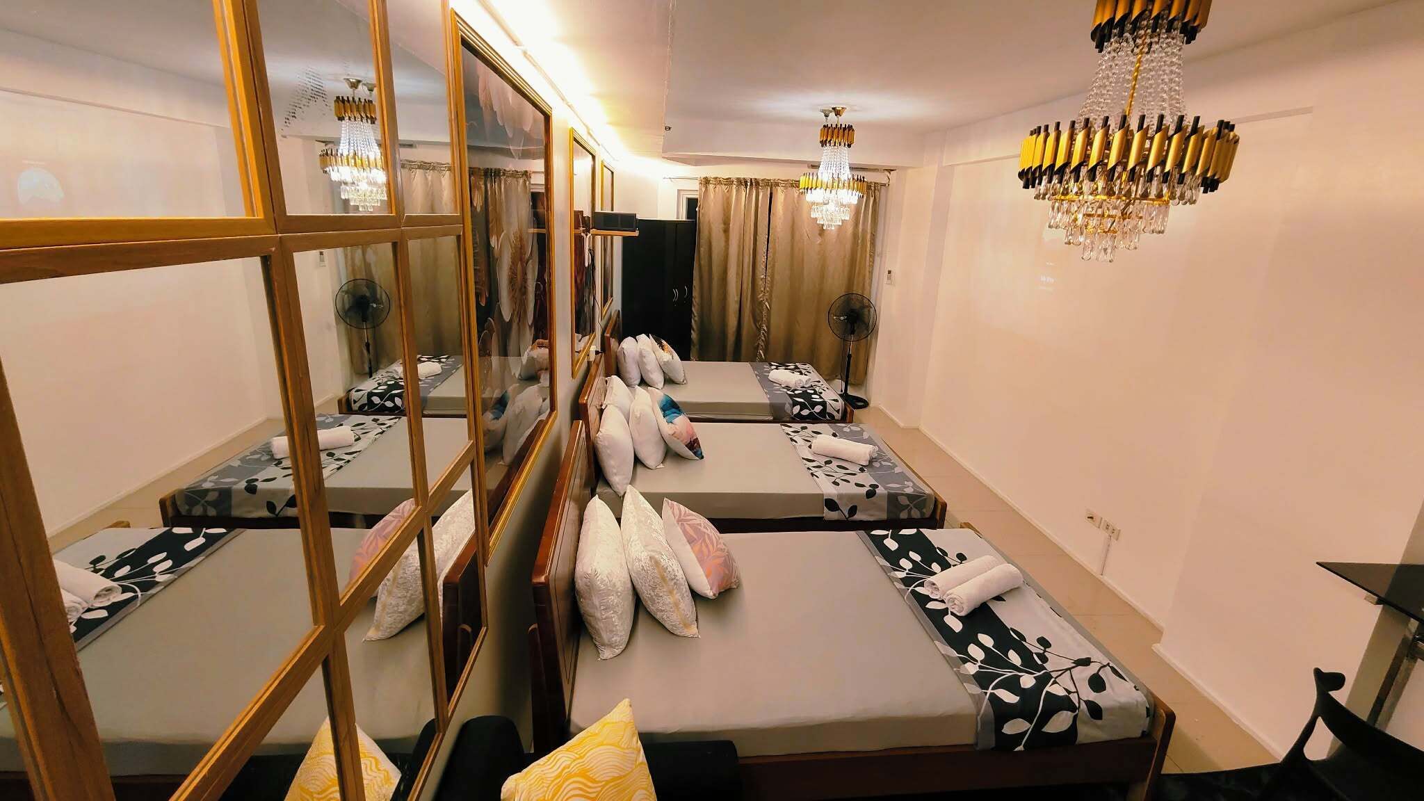 Une chambre d’hôtel avec un mur recouvert de miroirs, un lustre et plusieurs lits avec des serviettes.
