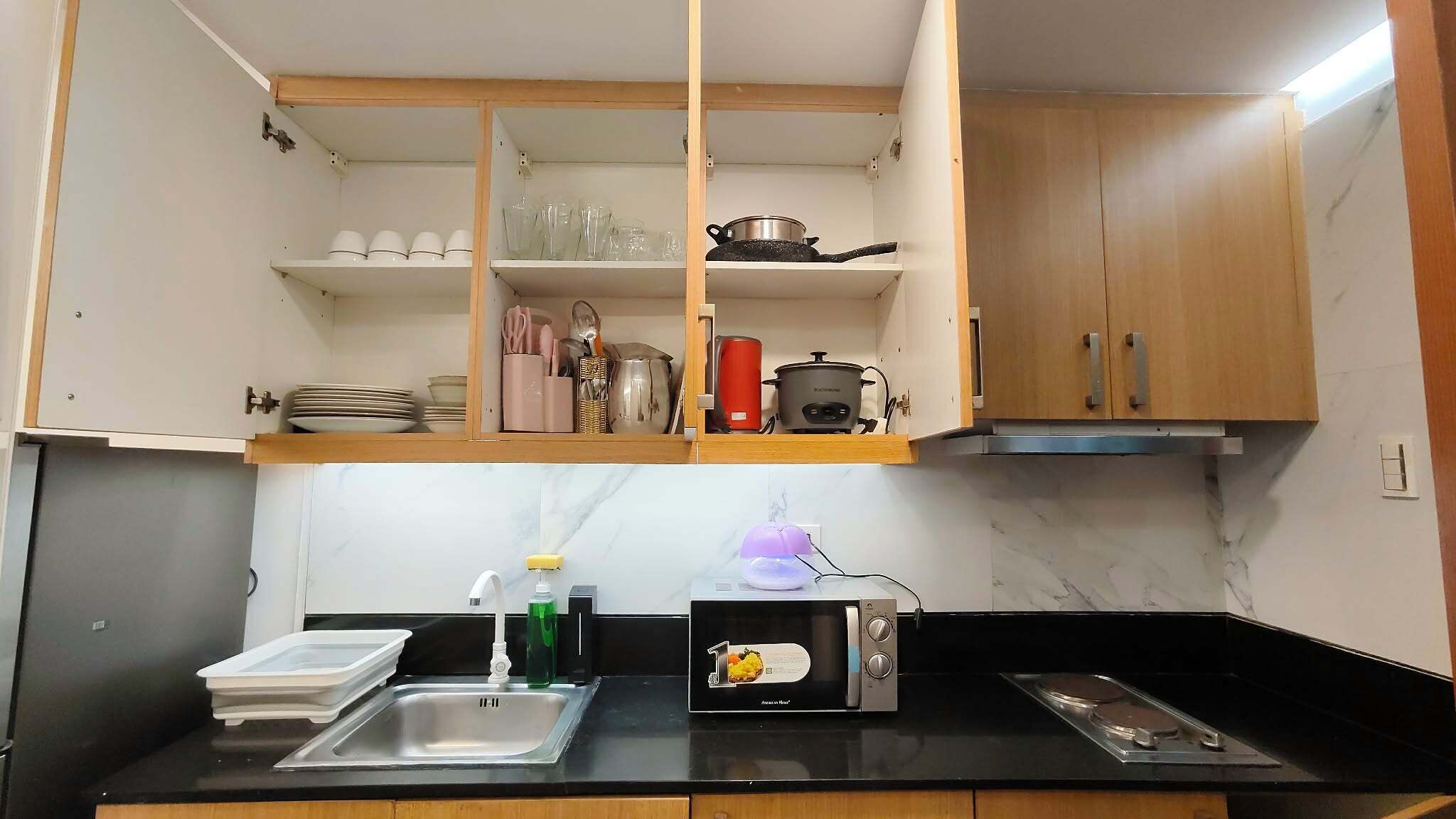 A kitchen with a black countertop, a stainless steel sink, a microwave, and wooden cabinets.