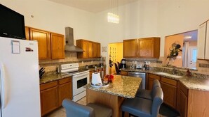 Cozinha com armários de madeira, bancadas de granito, forno embutido, geladeira e banquetas.