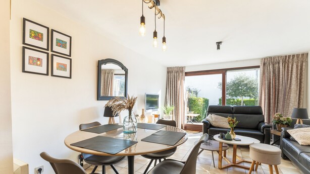 A modern living room with a dining area, large windows, and a black leather sofa. - 2 bedroom accommodation in Nieuwpoort (Nieuwpoort)
