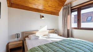 A bedroom with a wooden ceiling, a bed with a green quilt, a nightstand with a lamp, and a window with curtains. - 2 bedroom accommodation in Nieuwpoort (Nieuwpoort)