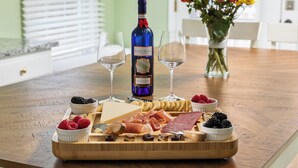 A wooden board with cheese, meats, and berries, a bottle of wine, and two glasses on a table. - Heart of Luray: Sauna, Hot Tub & Fire Pit (Luray)