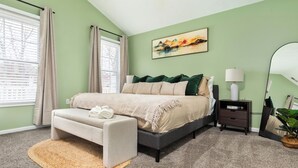A bedroom with a bed, a bedside table, a lamp, a window with curtains, and a painting on the wall. - Heart of Luray: Sauna, Hot Tub & Fire Pit (Luray)