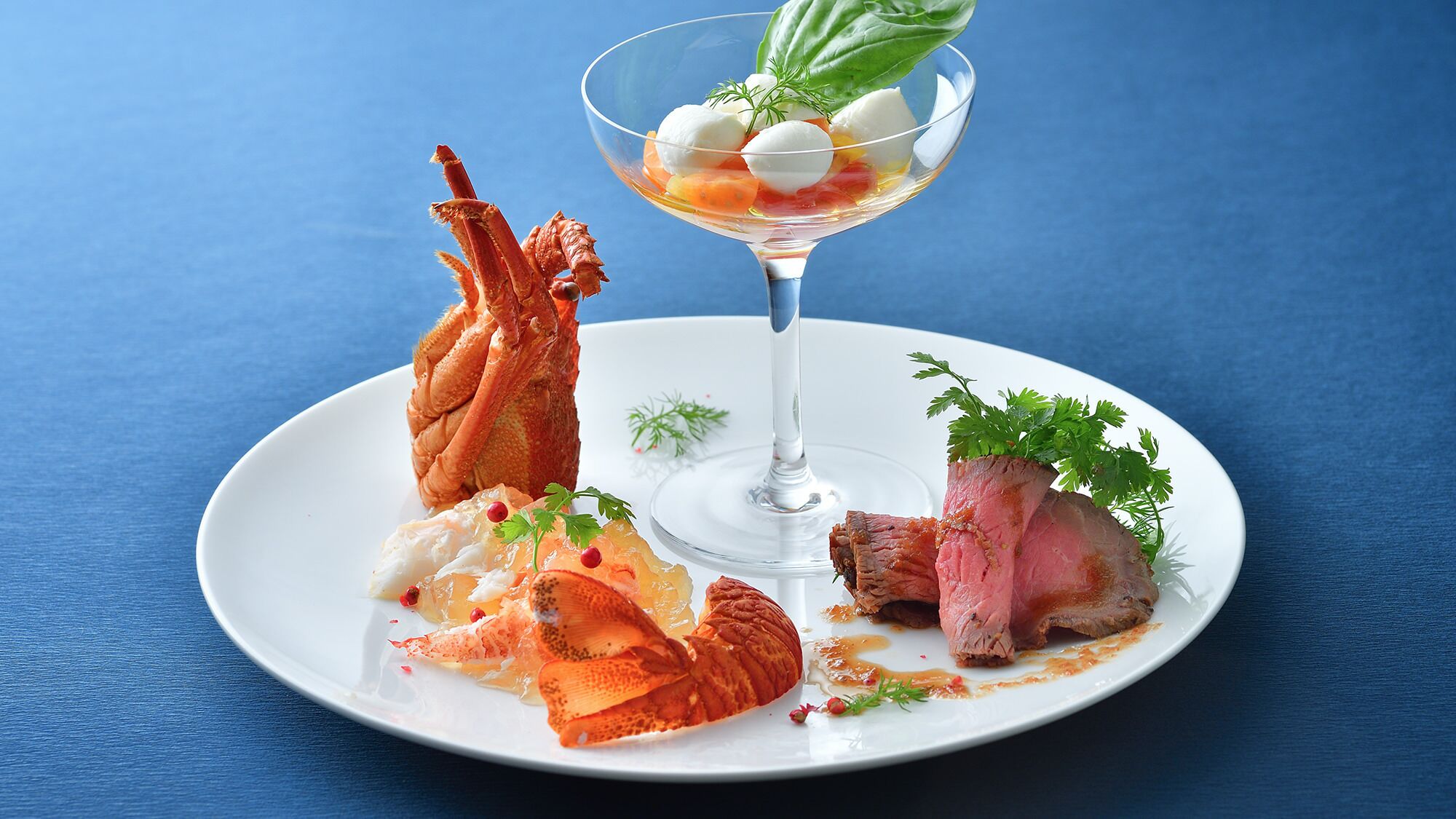 Un plato con langosta, una copa de vino blanco y un trozo de carne.