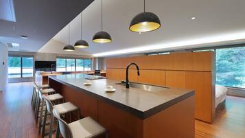 Una cocina moderna con una isla central, taburetes de bar, iluminación colgante y ventanas amplias.