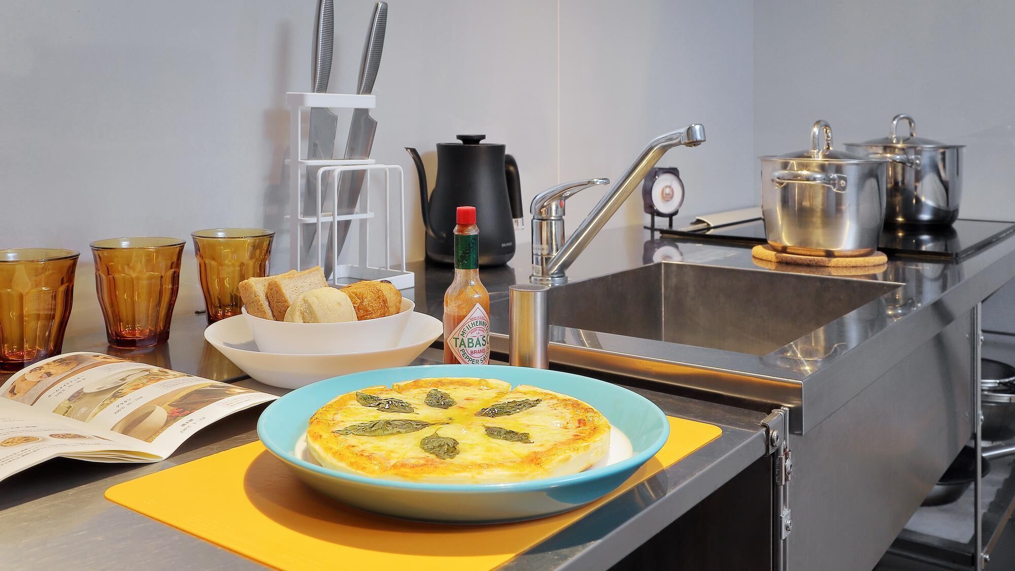 A kitchen with a stove, sink, and various kitchen items including a bowl of food, a book, and a bottle of sauce.