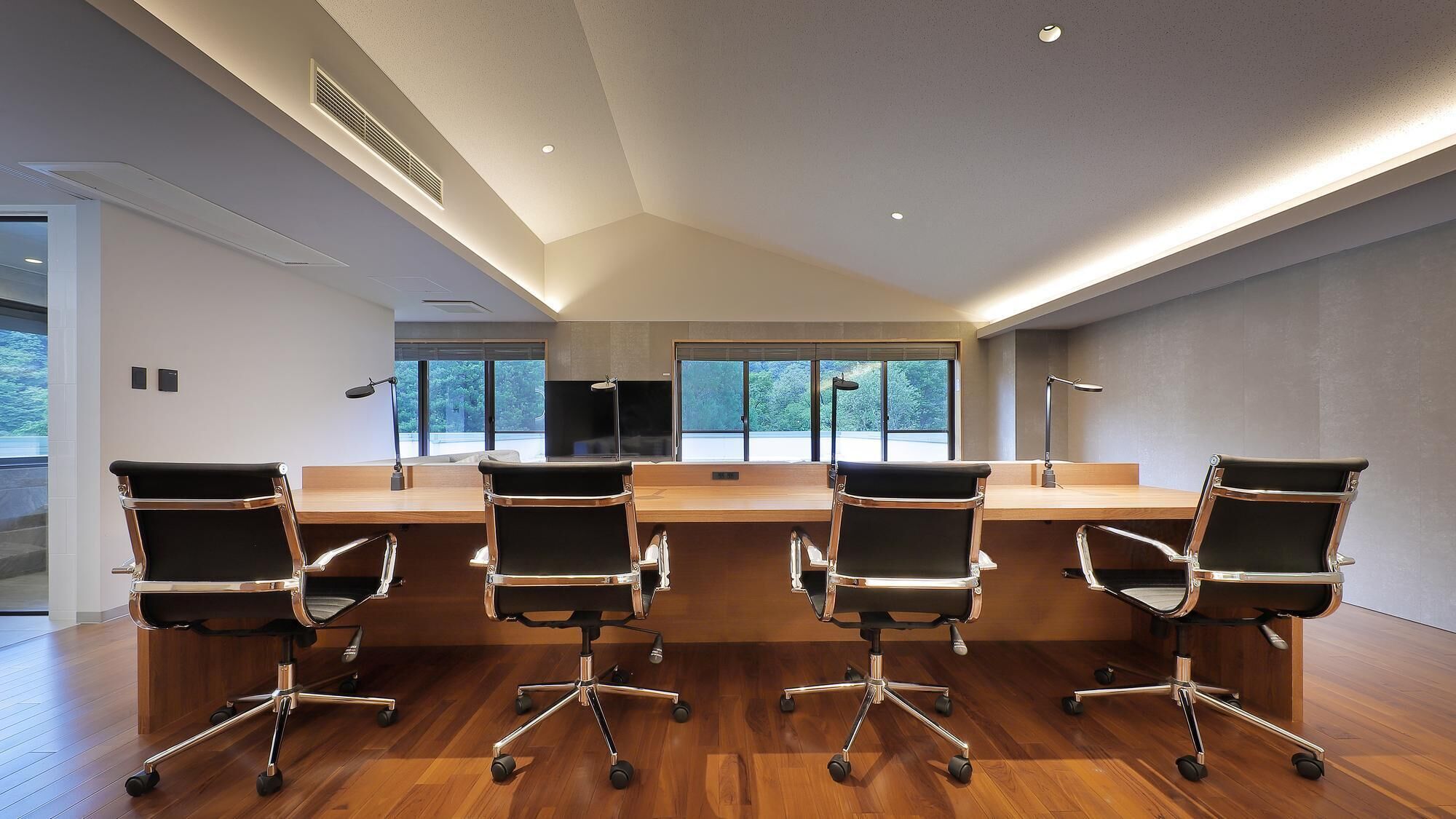 Een moderne vergaderruimte met een lange tafel, vier bureaustoelen en grote ramen.