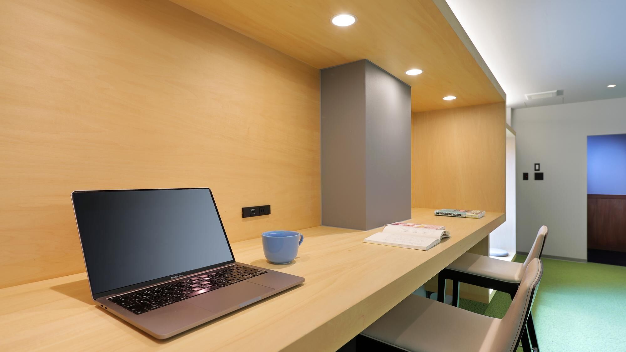 A modern office space with a laptop on a wooden desk, a blue mug, and a book.