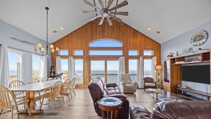 A spacious living area with a large wooden ceiling, a dining table with chairs, a leather sofa, and a television. - Sounds Good - Sound front home with stunning views and hot tub (Buxton)