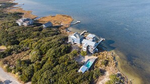 An aerial view of a coastal property with multiple buildings, a dock, and a clear view of the ocean. - Sounds Good - Sound front home with stunning views and hot tub (Buxton)