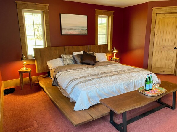 A bedroom with a large bed, two bedside tables with lamps, a wooden bench, and a door.