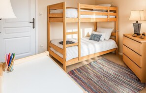 Ein Stockbett mit Holzrahmen, ein Schreibtisch mit Lampe und ein farbenfroher Teppich.