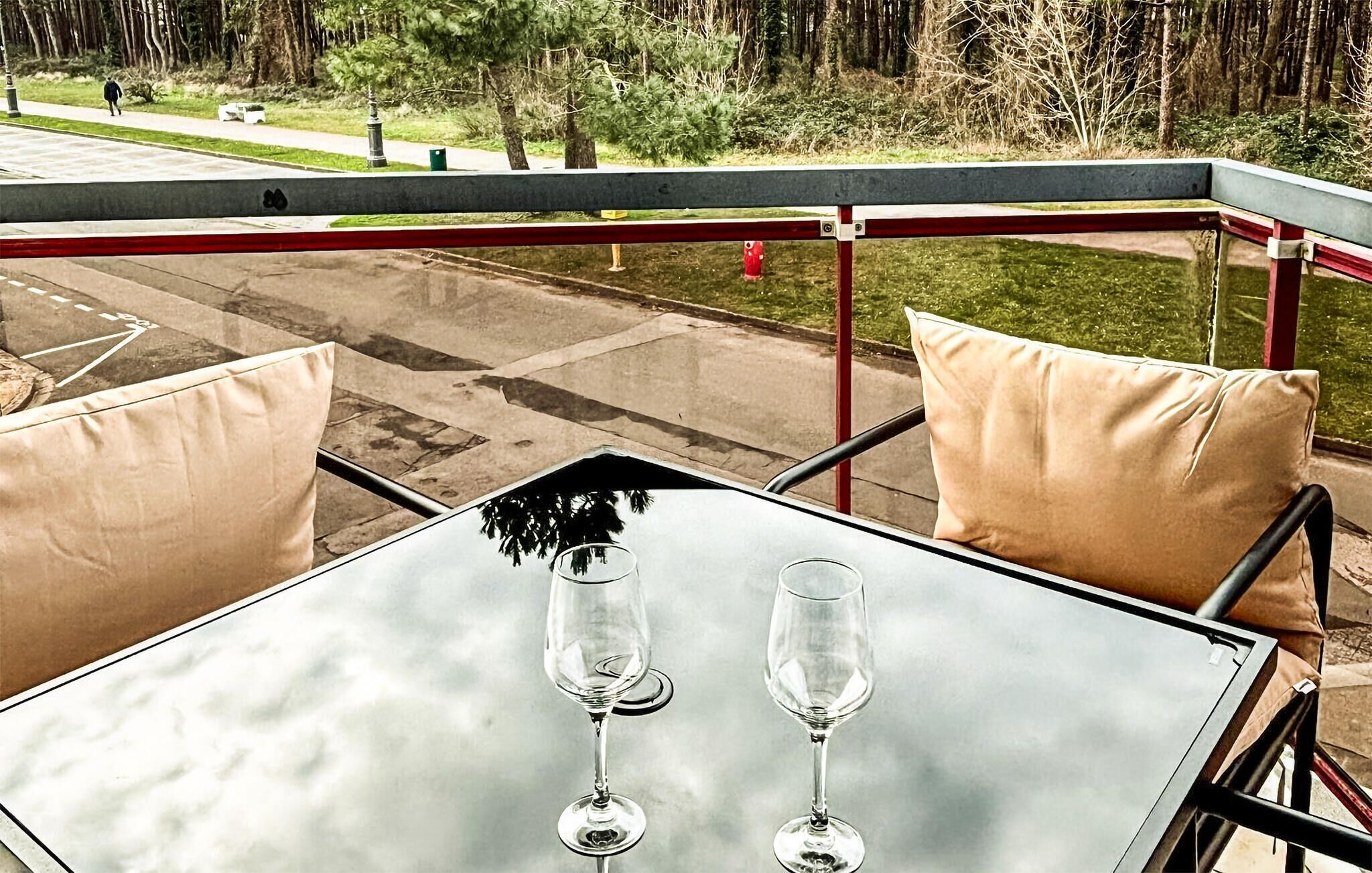 Ein Glastisch mit zwei Weingläsern auf einer Terrasse mit Außenbestuhlung.