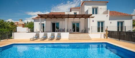 En modern villa med en swimmingpool, utomhusmöbler och en täckt uteplats.